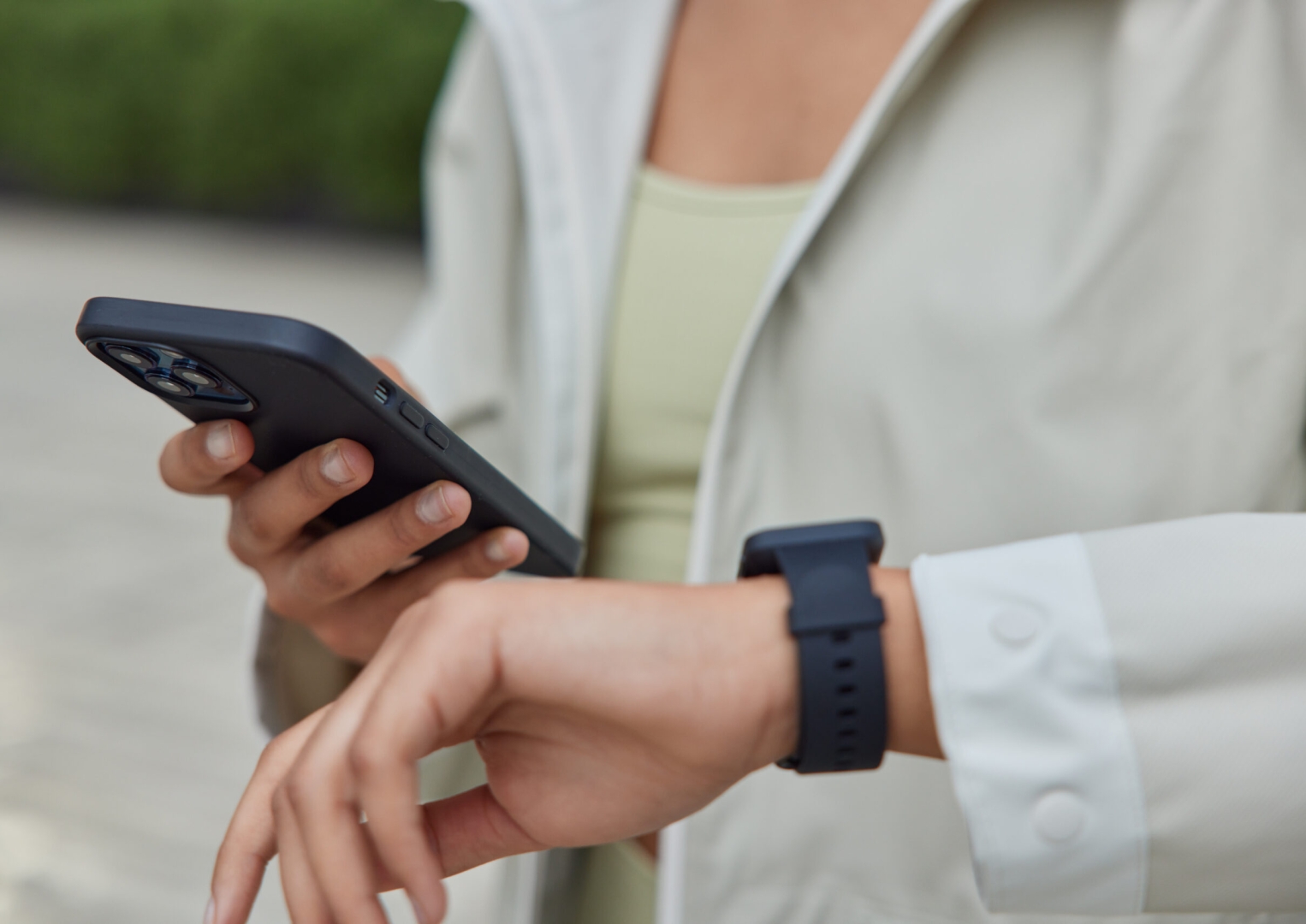 Cropped shot of unrecognizable woman holds modern smartphone and wearable smartwatch uses fitness app on wearable device to monitor workout performance leads healthy lifestyle poses outdoors